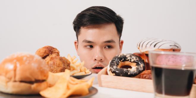 Young man having cravings for donuts, hamburger, chicken with fries.